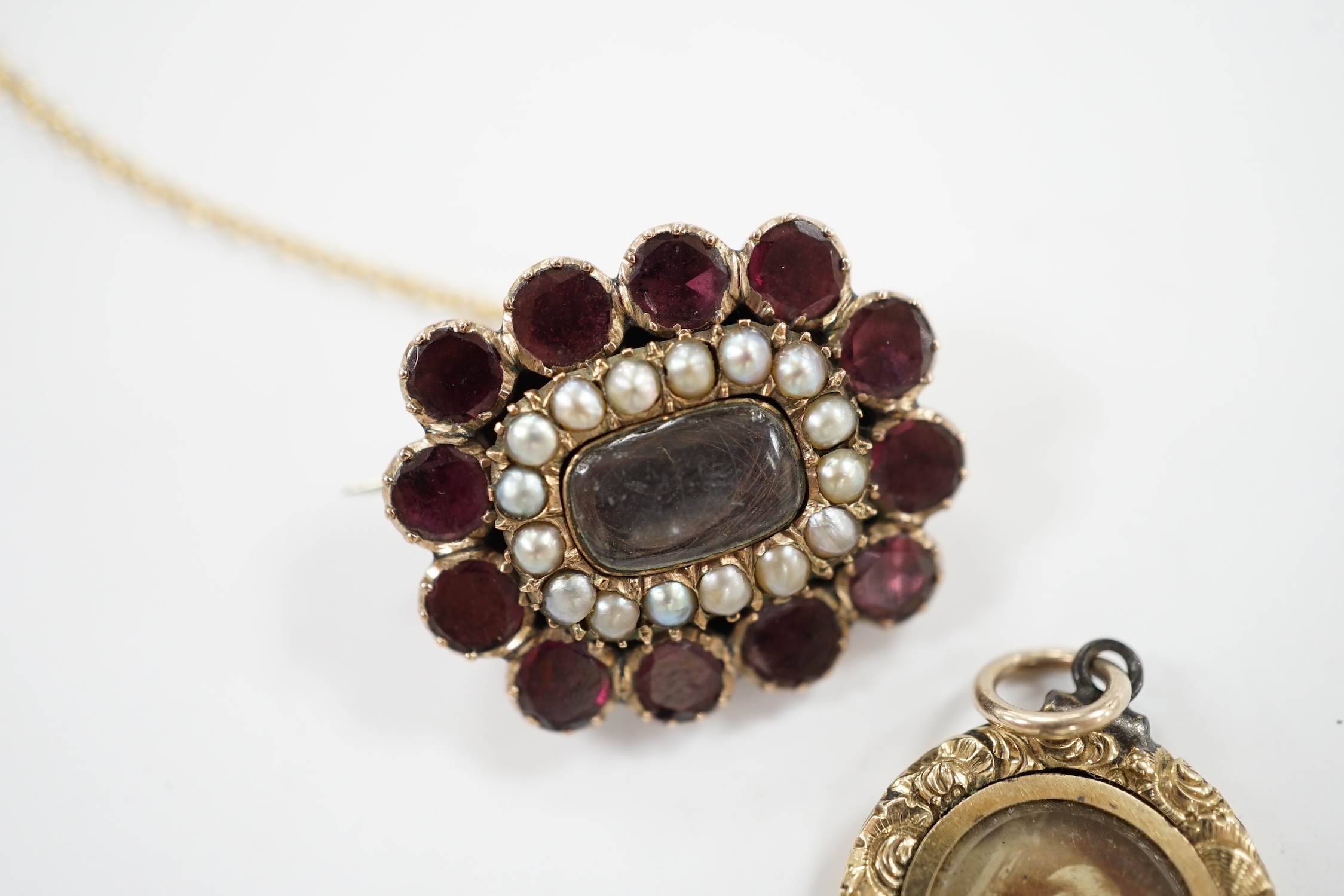 An early Victorian yellow metal, garnet and split pearl set mourning brooch, with engraved monogram, 23mm and a George IV mourning locket, inscribed 'Martha Lloyd, ob. 8th May, 1824 at 53'. Condition - fair